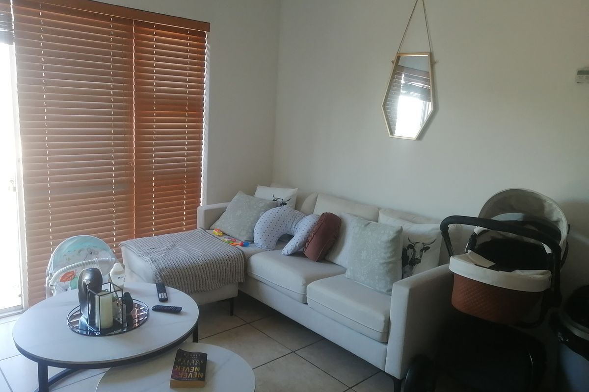 A bright living room featuring tiled flooring and large sliding glass doors fitted with wooden venetian blinds, providing natural light to the space.