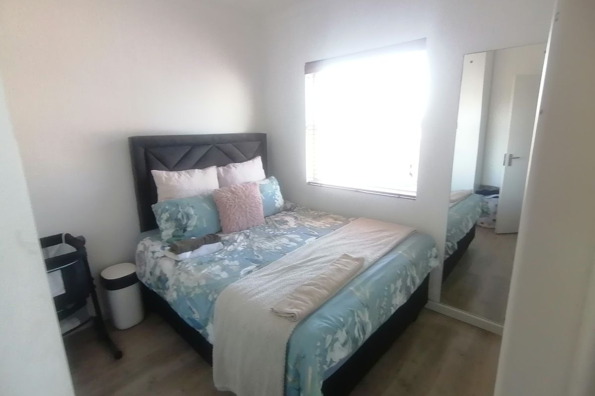 A bedroom featuring light-toned wood-look flooring, a large window for natural light, and a built-in mirrored wardrobe.