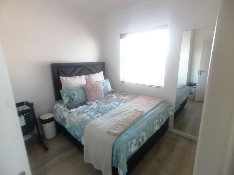 A bedroom featuring light-toned wood-look flooring, a large window for natural light, and a built-in mirrored wardrobe.
