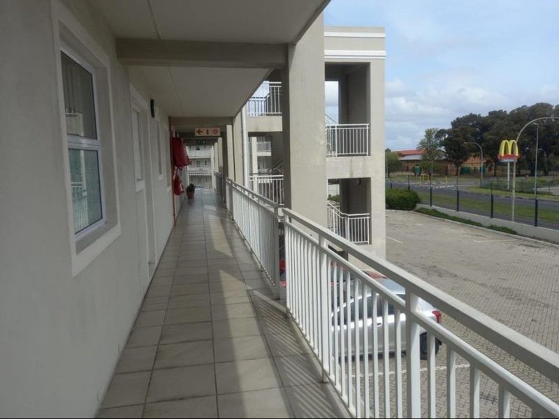 An exterior walkway or balcony area of an apartment complex, featuring tiled flooring and metal safety railings overlooking the parking area.