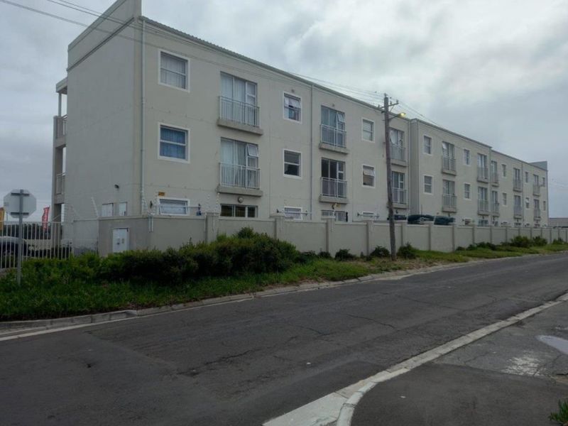 Exterior view of a multi-story apartment complex featuring a perimeter wall, security fencing, and multiple balconies.