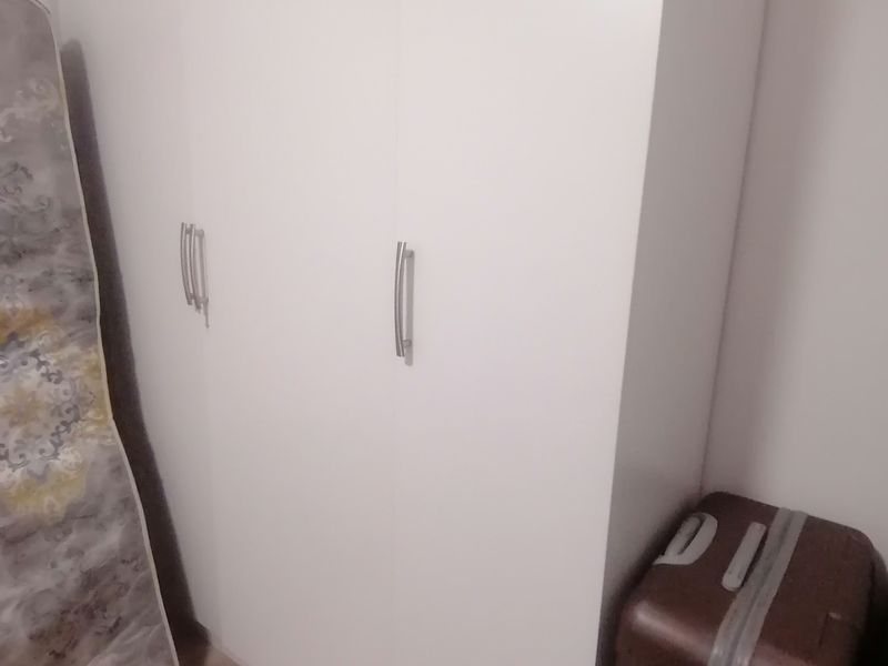 A bedroom featuring a built-in white wardrobe with modern silver handles and light-toned laminate flooring.