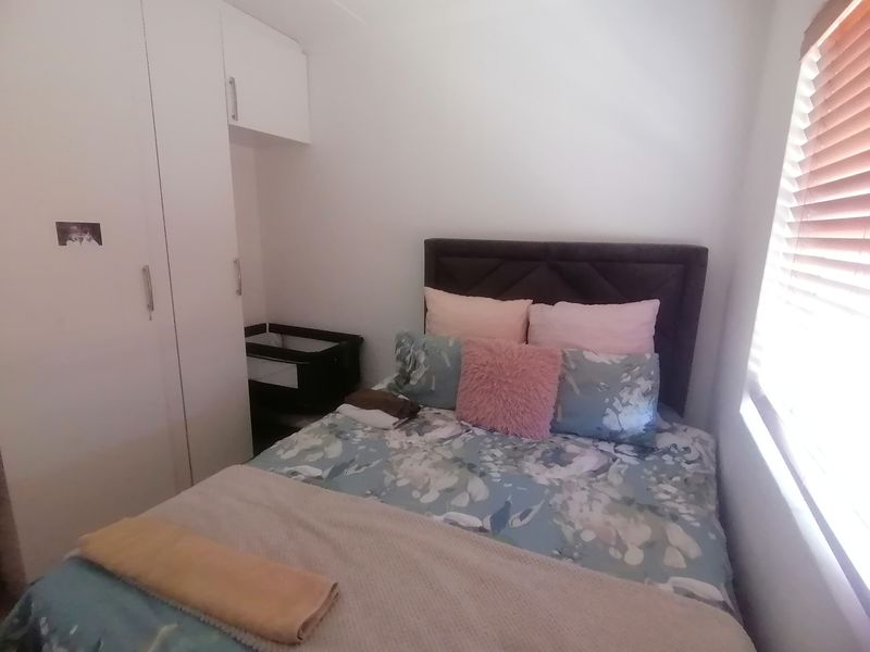 A compact bedroom featuring built-in white cabinetry and a window with fitted wooden blinds.