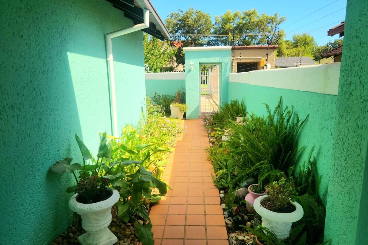 A well-maintained side garden pathway featuring terracotta tiling, bordered by vibrant green walls and a secure pedestrian gate.