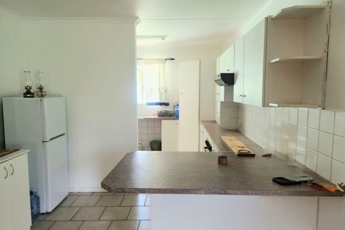 A functional kitchen featuring laminate countertops, tiled backsplash, and built-in cabinetry, with an adjacent scullery area visible in the background.