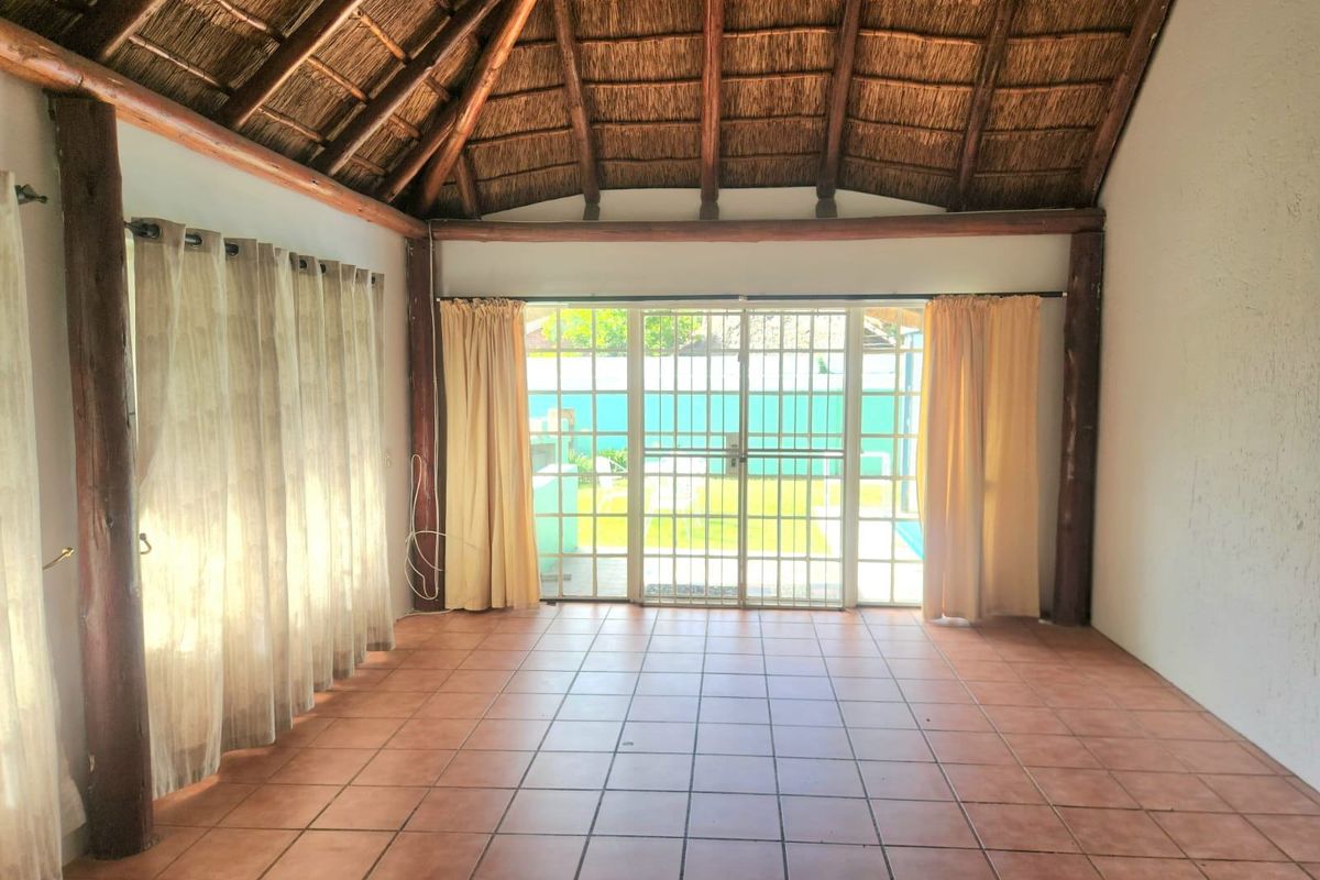 Spacious living area featuring a high vaulted thatched ceiling with exposed timber beams, ceramic tiled flooring, and sliding glass doors leading to the garden.