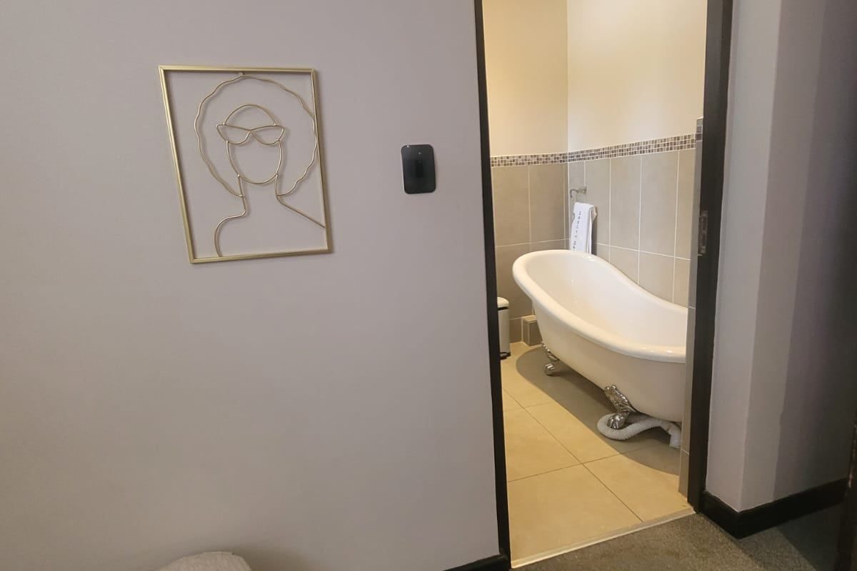 A view into a bathroom featuring a classic clawfoot bathtub, neutral wall tiling with a decorative border, and recessed ceiling lighting.