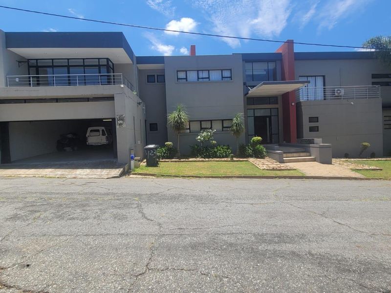 Modern multi-level residential facade featuring a double garage, upper-level balcony, and a paved entrance area with contemporary architectural styling.