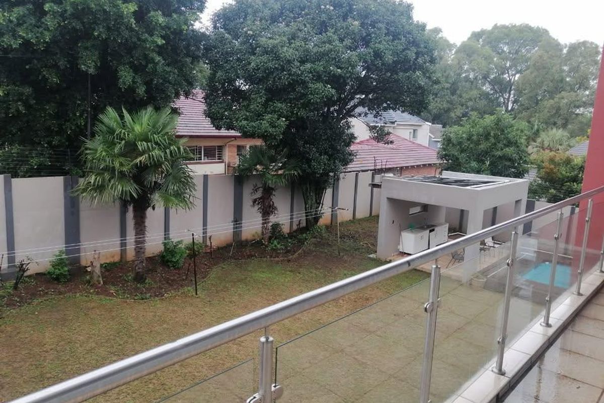 Rear view from a balcony overlooking a garden, swimming pool, and covered patio area with a built-in braai.