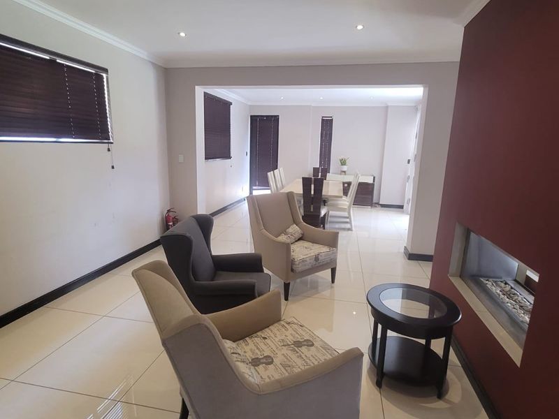 Spacious open-plan living and dining area featuring large format floor tiles, a modern built-in fireplace, and recessed lighting throughout.