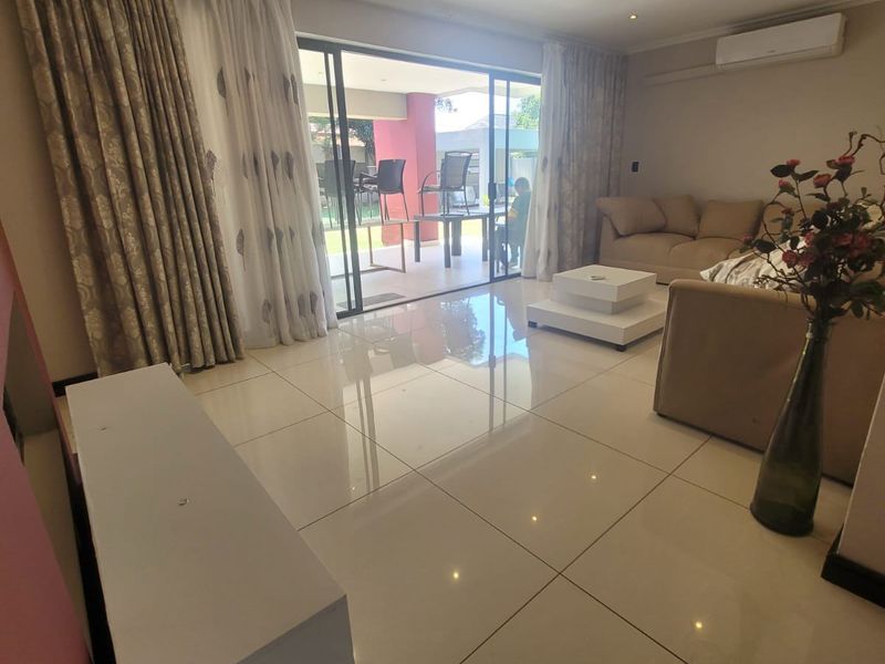 Spacious living room featuring polished porcelain floor tiles, recessed downlighting, and large sliding glass doors providing seamless access to the outdoor patio area.