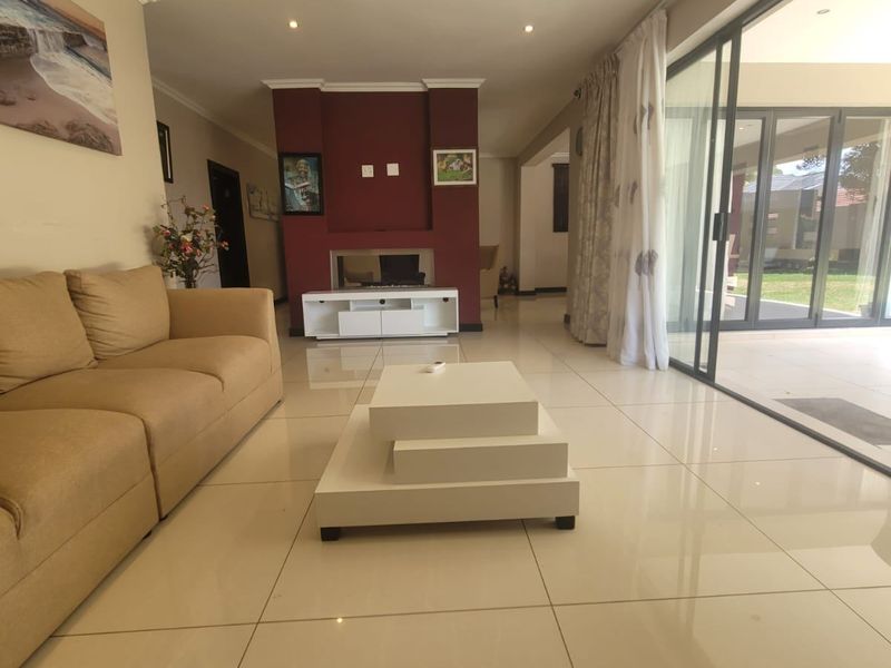 Spacious living room featuring large format floor tiles, a central built-in fireplace, and expansive sliding glass doors providing seamless access to the outdoor patio area.