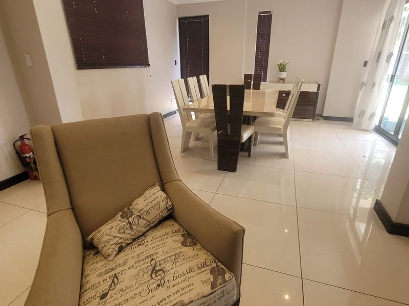 A bright and spacious dining area featuring large format porcelain floor tiles, recessed downlighting, and sliding glass doors leading to the exterior.