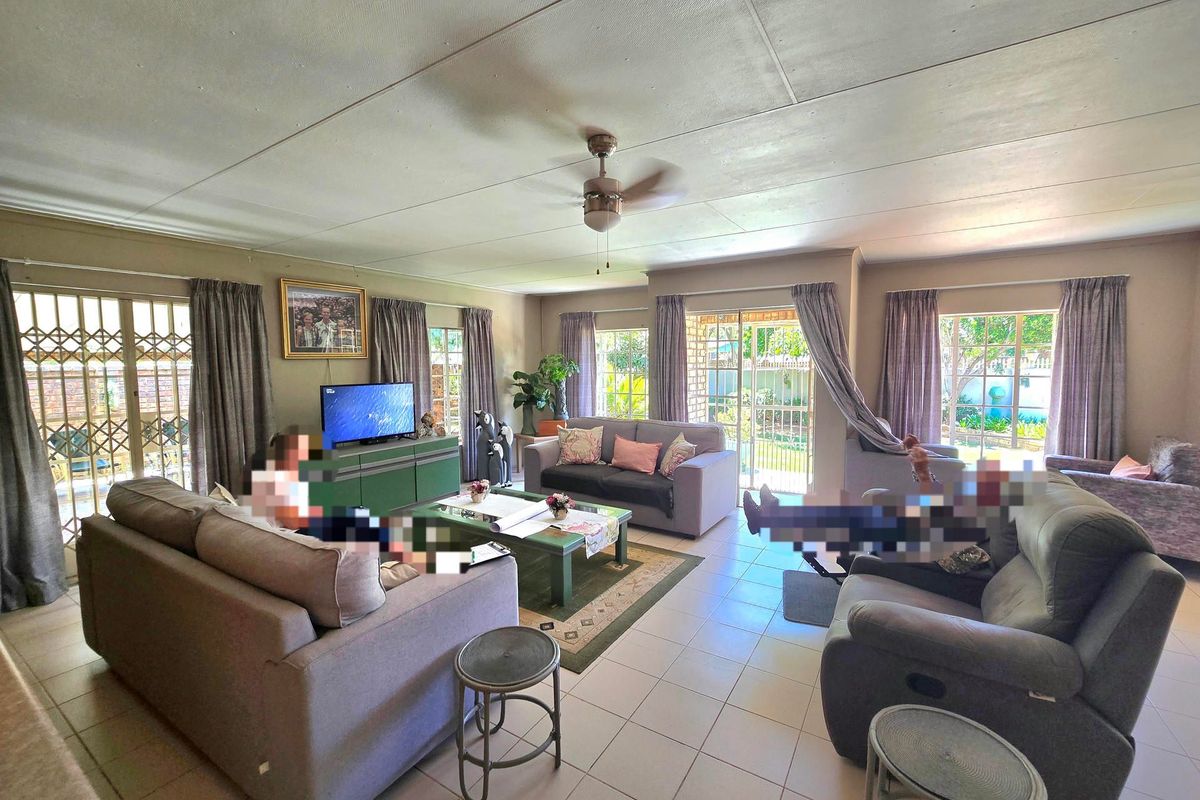 Spacious living room featuring tiled flooring, ceiling fan, and multiple sliding glass doors providing access to the garden area.