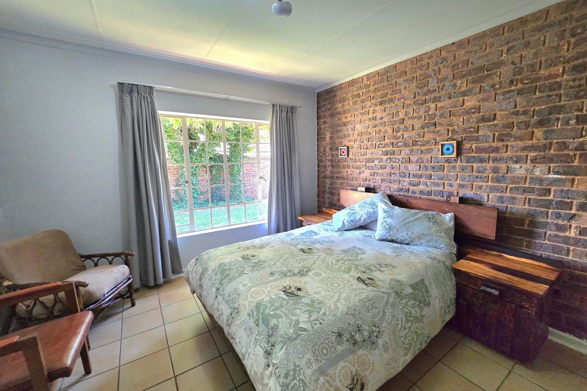 A bedroom featuring a rustic exposed brick feature wall, tiled flooring, and a large window providing natural light and garden views.