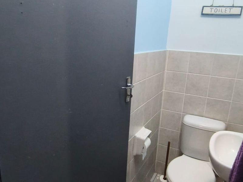 A compact bathroom featuring a standard toilet, wall-mounted basin, and neutral wall tiling.