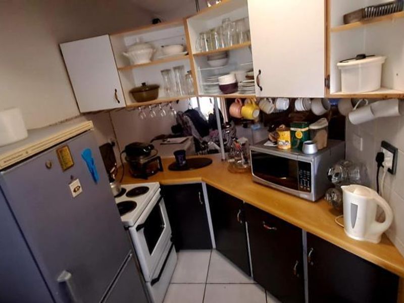 Compact kitchen featuring dark lower cabinetry, light upper shelving, tiled backsplash, and built-in stove, offering a functional layout for an apartment setting.