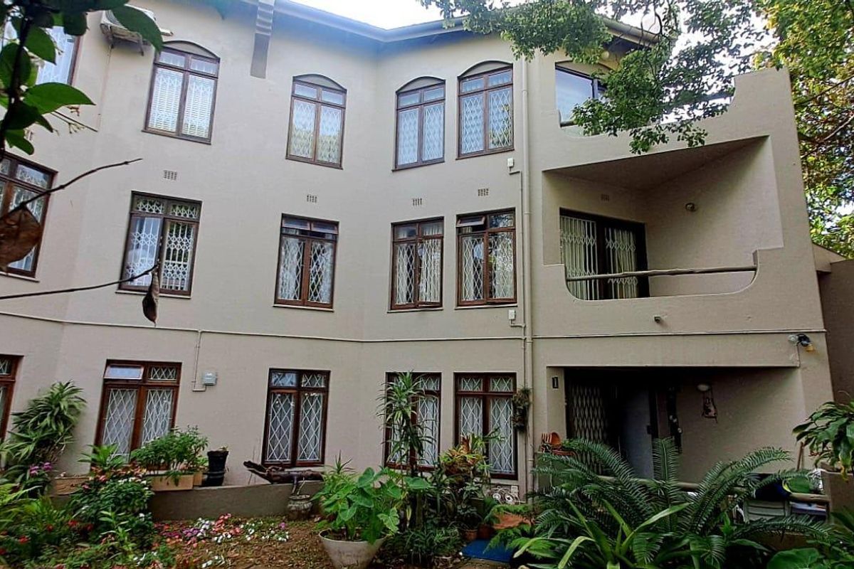 A view of the rear exterior facade of the apartment building, featuring multiple windows with security bars and a covered balcony area.