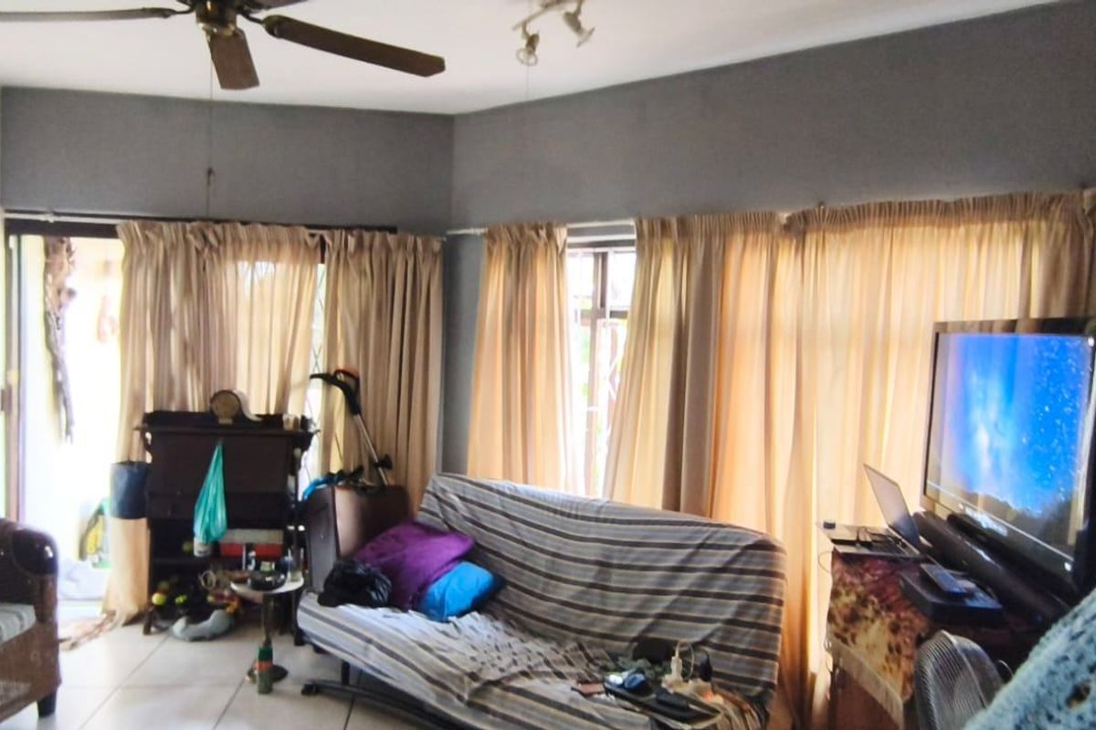 A living room area featuring tiled flooring, a ceiling fan, and large windows with curtains providing access to an outdoor space.