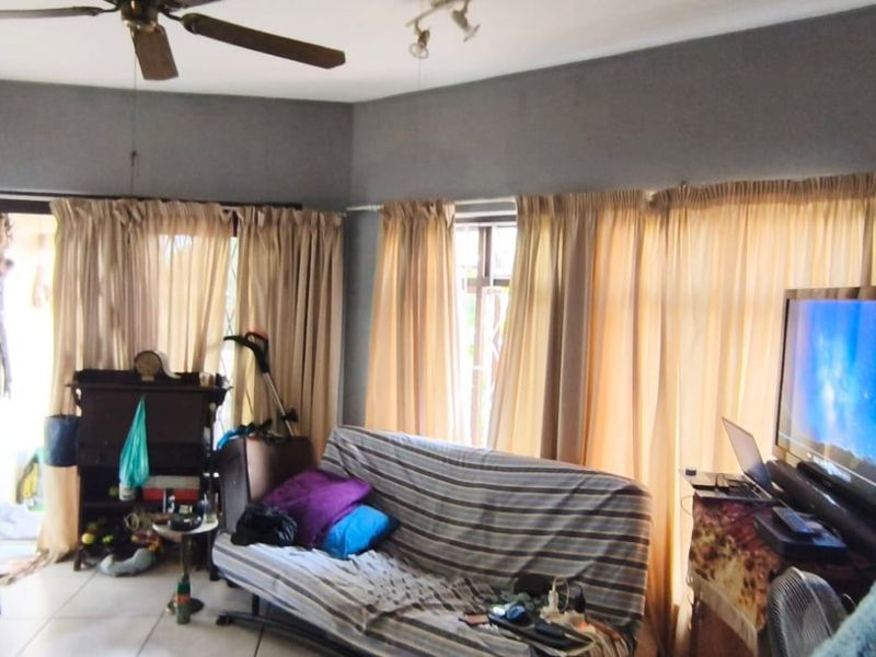 A living room area featuring tiled flooring, a ceiling fan, and large windows with curtains providing access to an outdoor space.