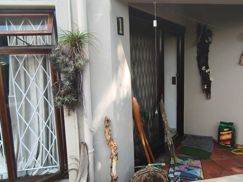 A covered patio area featuring tiled flooring, dark timber-framed windows with security bars, and sliding glass door access to the interior.