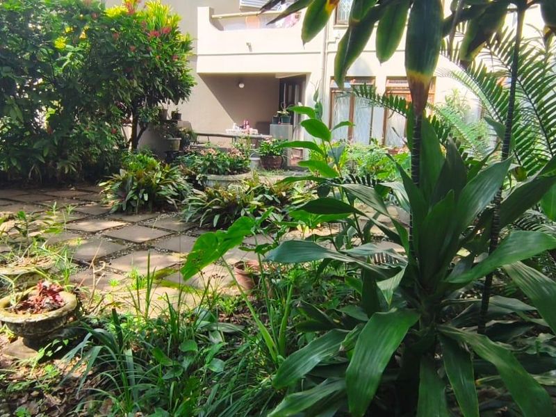 A lush, landscaped garden area featuring paved walkways and established greenery, providing a private outdoor space adjacent to the apartment building.