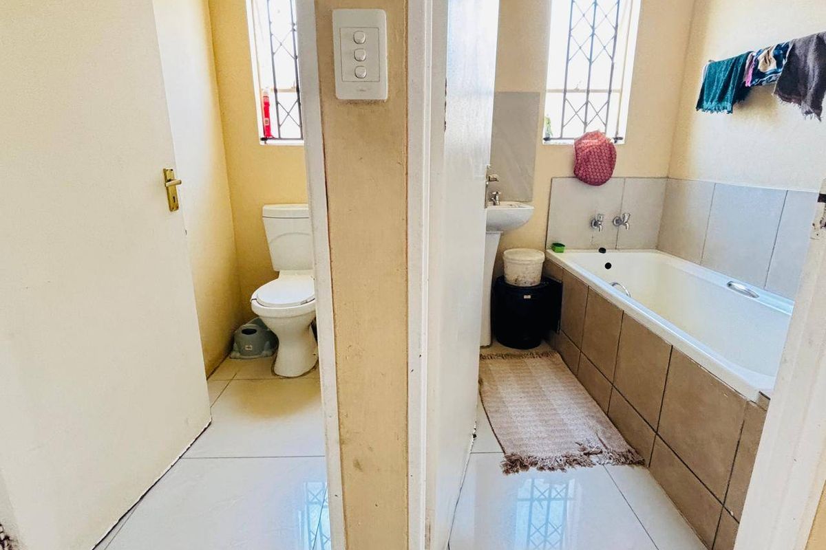 A functional bathroom featuring a separate toilet area, pedestal basin, and a tiled bathtub with security bars on the windows.