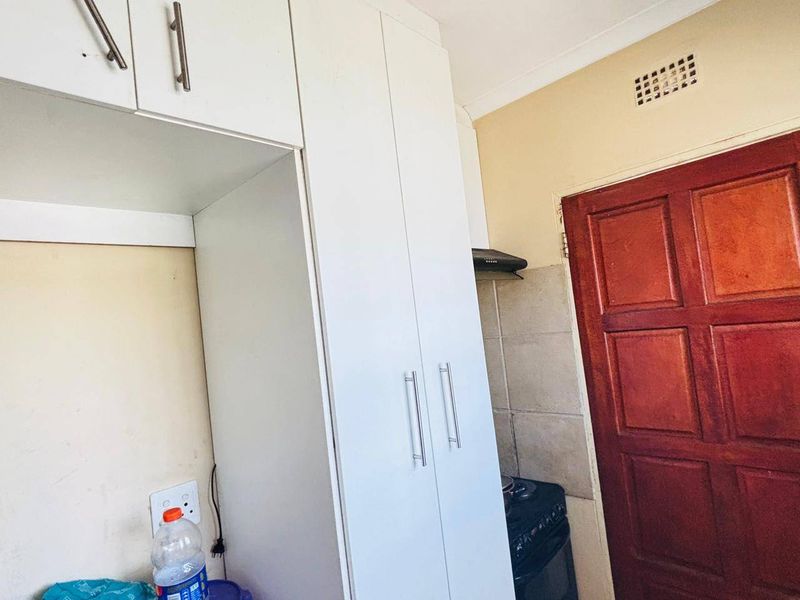 A compact kitchen area featuring white built-in cabinetry, a stove with an extractor fan, and a wooden door.