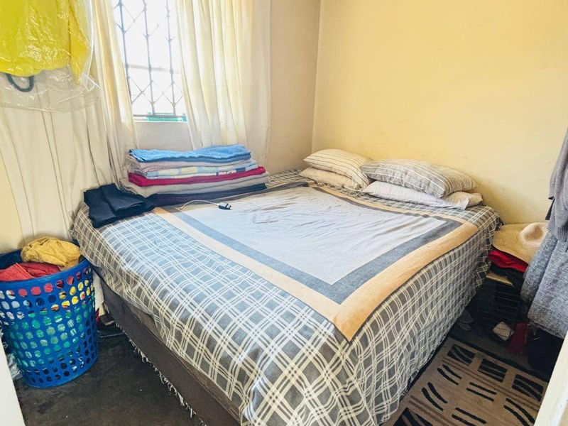 A compact bedroom featuring a window with security bars and basic finishes, suitable for a single bed setup.