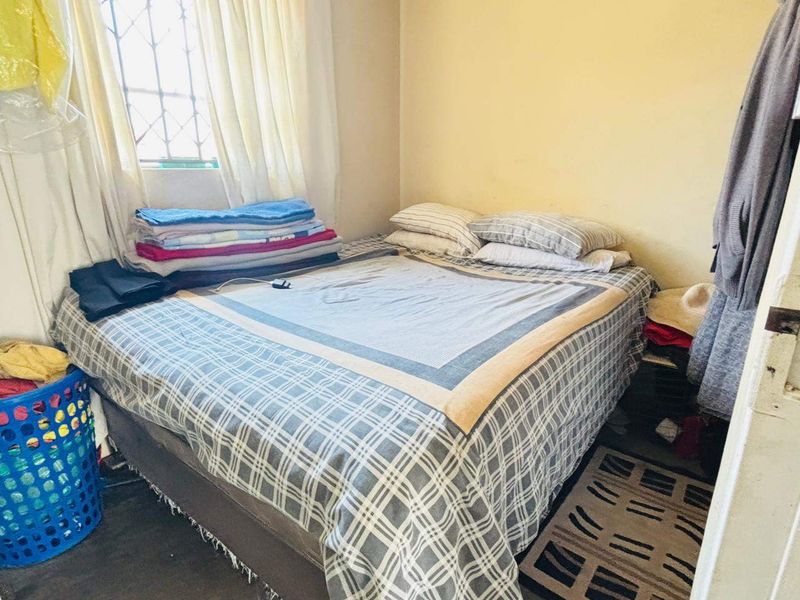 A compact bedroom featuring a window with security bars and neutral wall finishes, offering a functional space for rest.