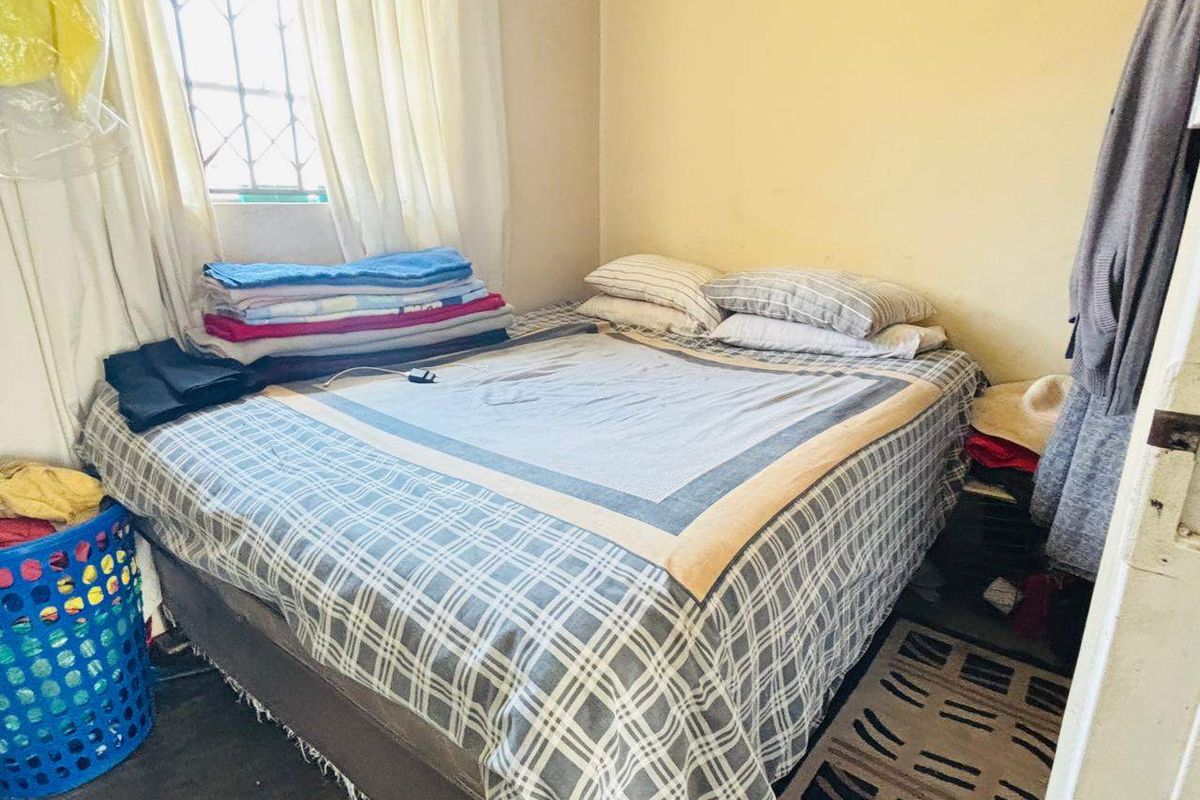 A compact bedroom featuring a window with security bars and neutral wall finishes, offering a functional space for rest.