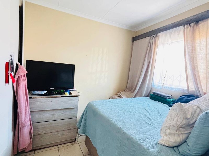A functional bedroom featuring tiled flooring, a window with security bars, and coved ceiling detailing.