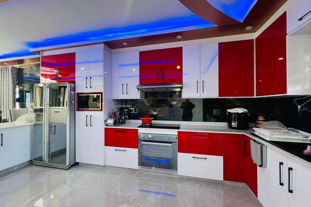 Modern kitchen featuring high-gloss red and white cabinetry, integrated appliances, stone countertops, and ambient LED ceiling lighting.