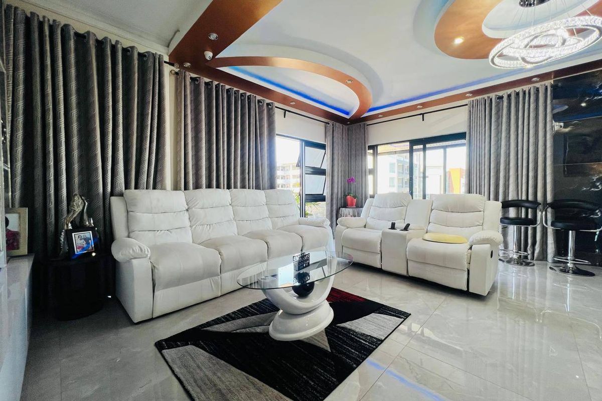 Modern living room featuring a decorative recessed ceiling with integrated LED lighting, polished porcelain floor tiles, and large sliding glass doors for natural light.