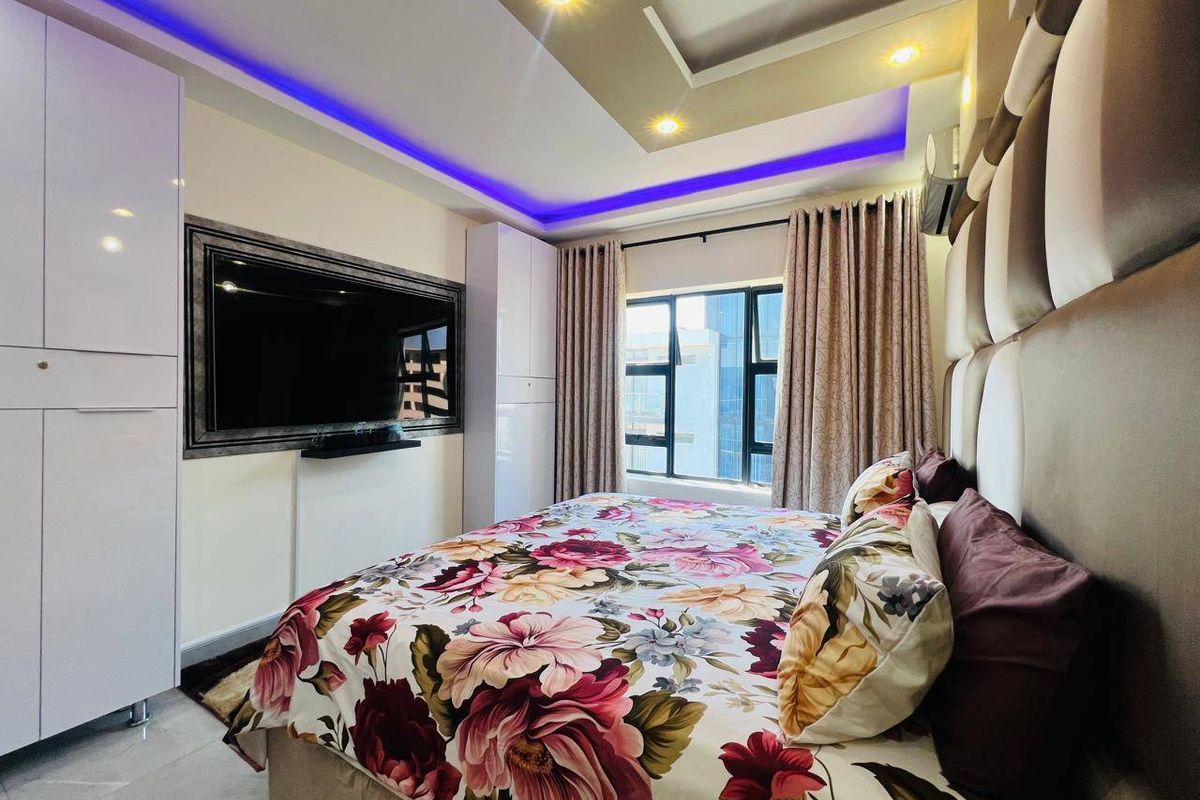 Modern bedroom featuring built-in high-gloss wardrobes, a custom upholstered headboard wall, and a recessed ceiling with integrated LED accent lighting.