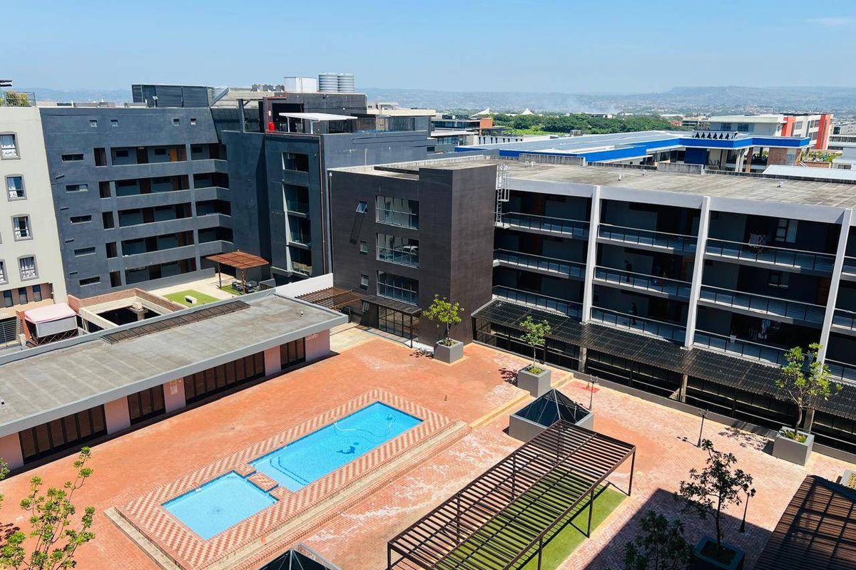 Aerial view of a modern apartment complex featuring a central courtyard with a swimming pool, paved areas, and pergolas.