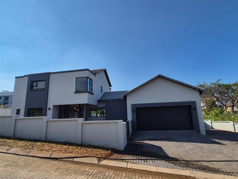 Modern double-storey residential property featuring a paved driveway, double garage, and secure boundary walling in a contemporary architectural style.