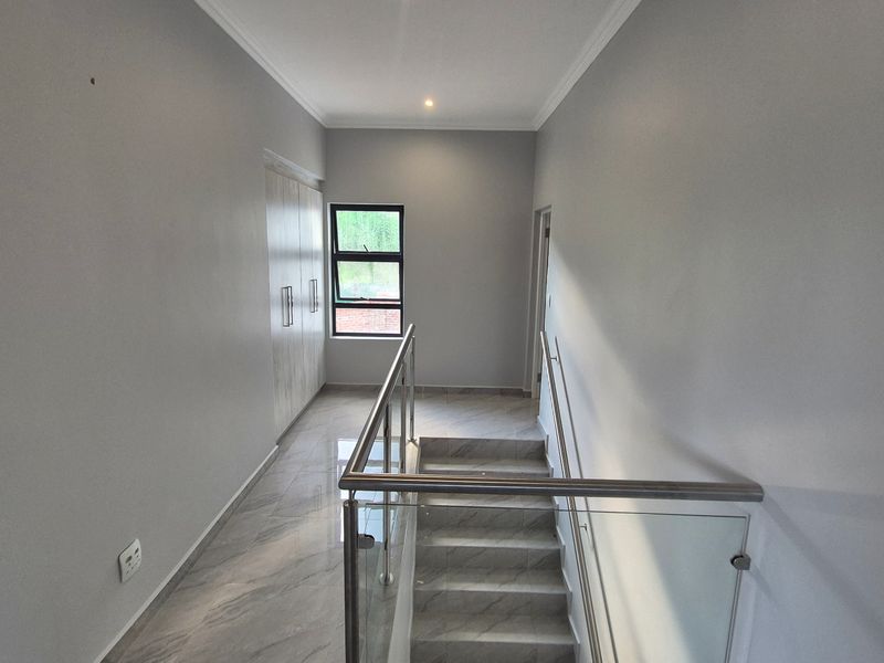 A bright, modern upstairs landing area featuring sleek tiled flooring, a contemporary glass balustrade, and built-in storage cupboards.