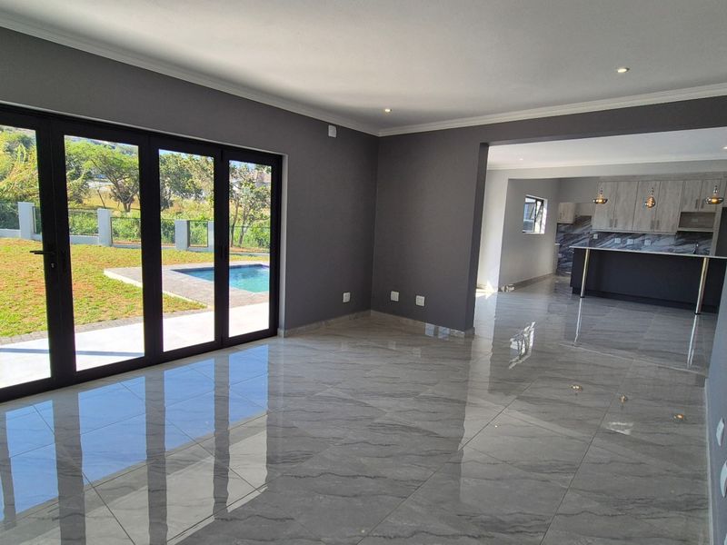 Spacious open-plan living area featuring polished marble-look floor tiles, modern recessed lighting, and seamless access to the outdoor pool area through large stacker doors.