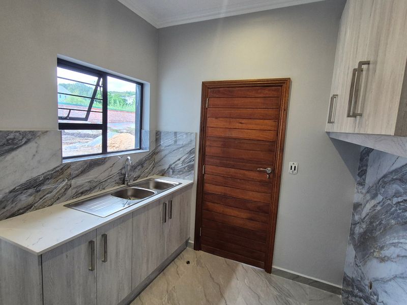 A modern, clean scullery featuring marble-look splashbacks, double stainless steel sink, ample built-in cabinetry, and tiled flooring.