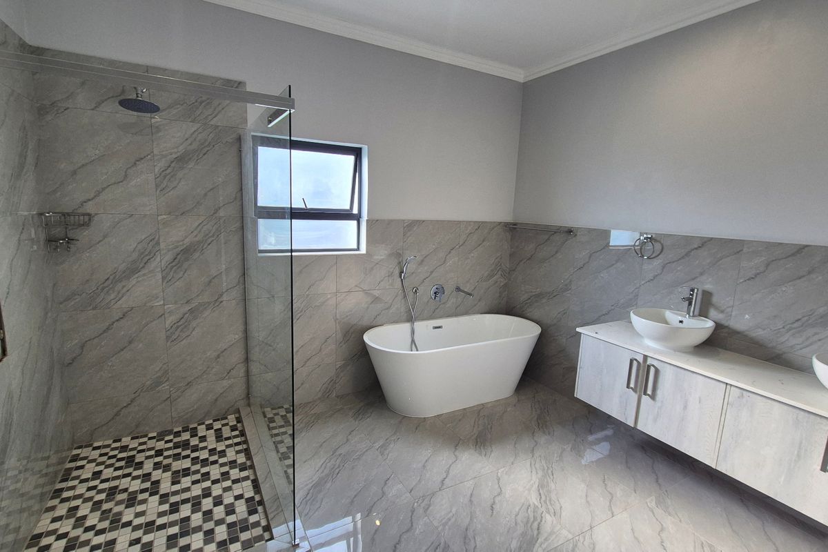 Modern bathroom featuring a freestanding bathtub, glass-enclosed shower, and dual vanity with wall-mounted cabinetry, finished with contemporary grey marble-look tiling.