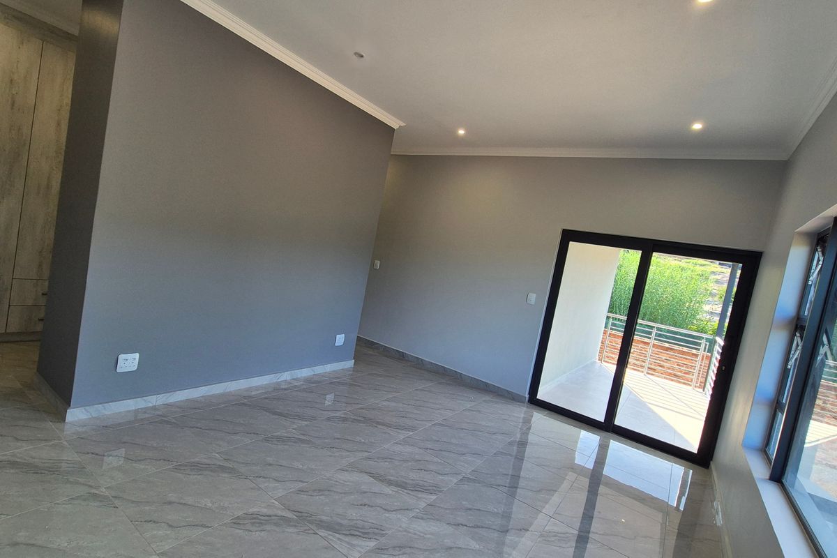 A spacious, modern bedroom featuring polished porcelain tiles, built-in cupboards, and a sliding glass door leading to an outdoor balcony.