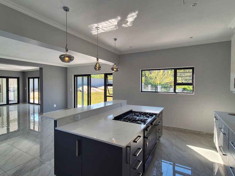 Modern open-plan kitchen and living area featuring a central island with gas hob, stone countertops, sleek cabinetry, and large sliding doors leading to the garden.