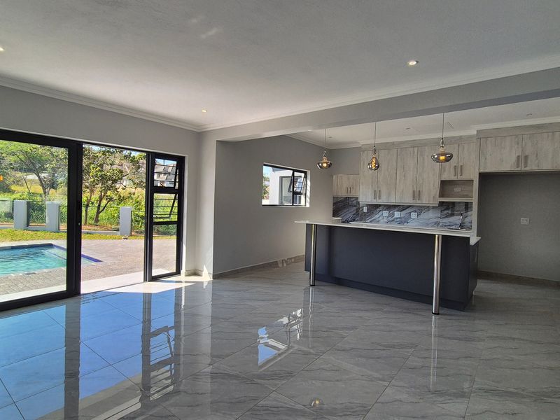 Spacious open-plan living and kitchen area featuring modern cabinetry, stone countertops, large porcelain tiles, and seamless access to the outdoor pool area.