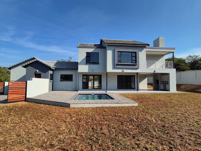 Rear view of a modern double-story house featuring a swimming pool, paved patio, balcony, and a built-in outdoor braai area.