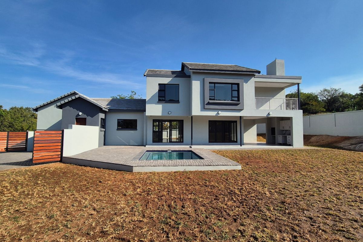 Rear view of a modern double-story house featuring a swimming pool, paved patio, balcony, and a built-in outdoor braai area.