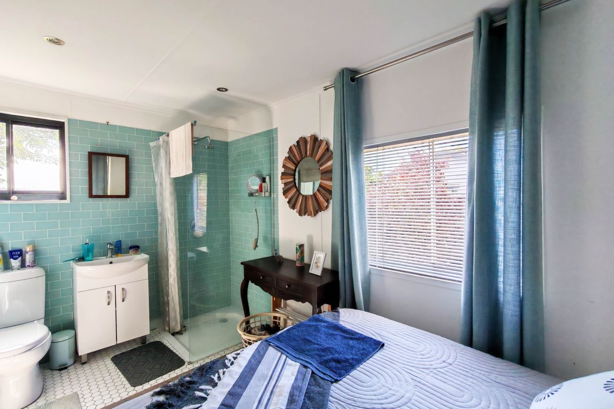 A bedroom featuring an integrated en-suite bathroom with a glass shower enclosure, vanity unit, and stylish teal subway tiling.