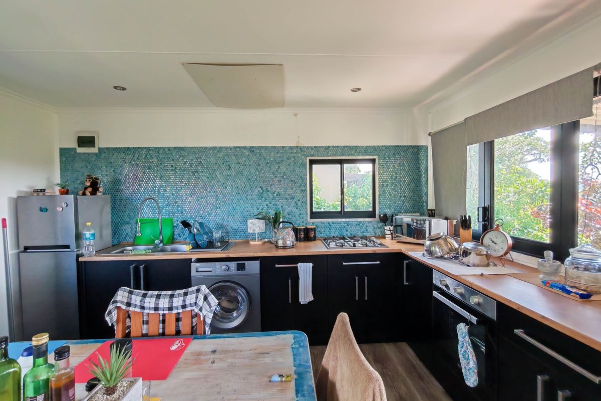 Functional kitchen featuring dark cabinetry, timber countertops, a striking blue mosaic tile backsplash, and integrated appliances including a gas hob and oven.