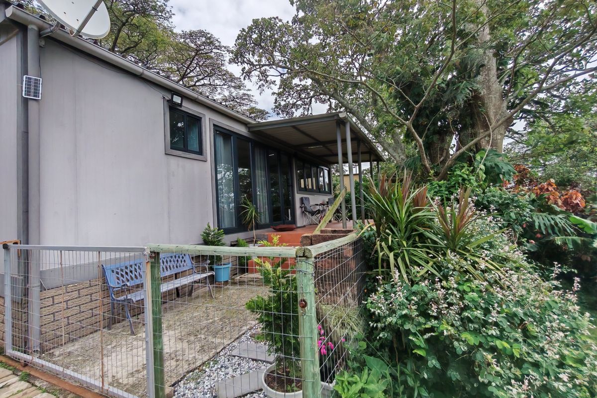 Rear exterior view of the property featuring a covered patio area, sliding glass doors, and established garden surroundings with security fencing.