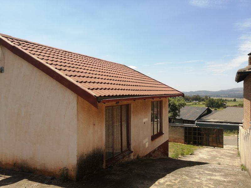 Rear view of the property showing a tiled roof, concrete driveway, and exterior walls requiring maintenance and repainting.